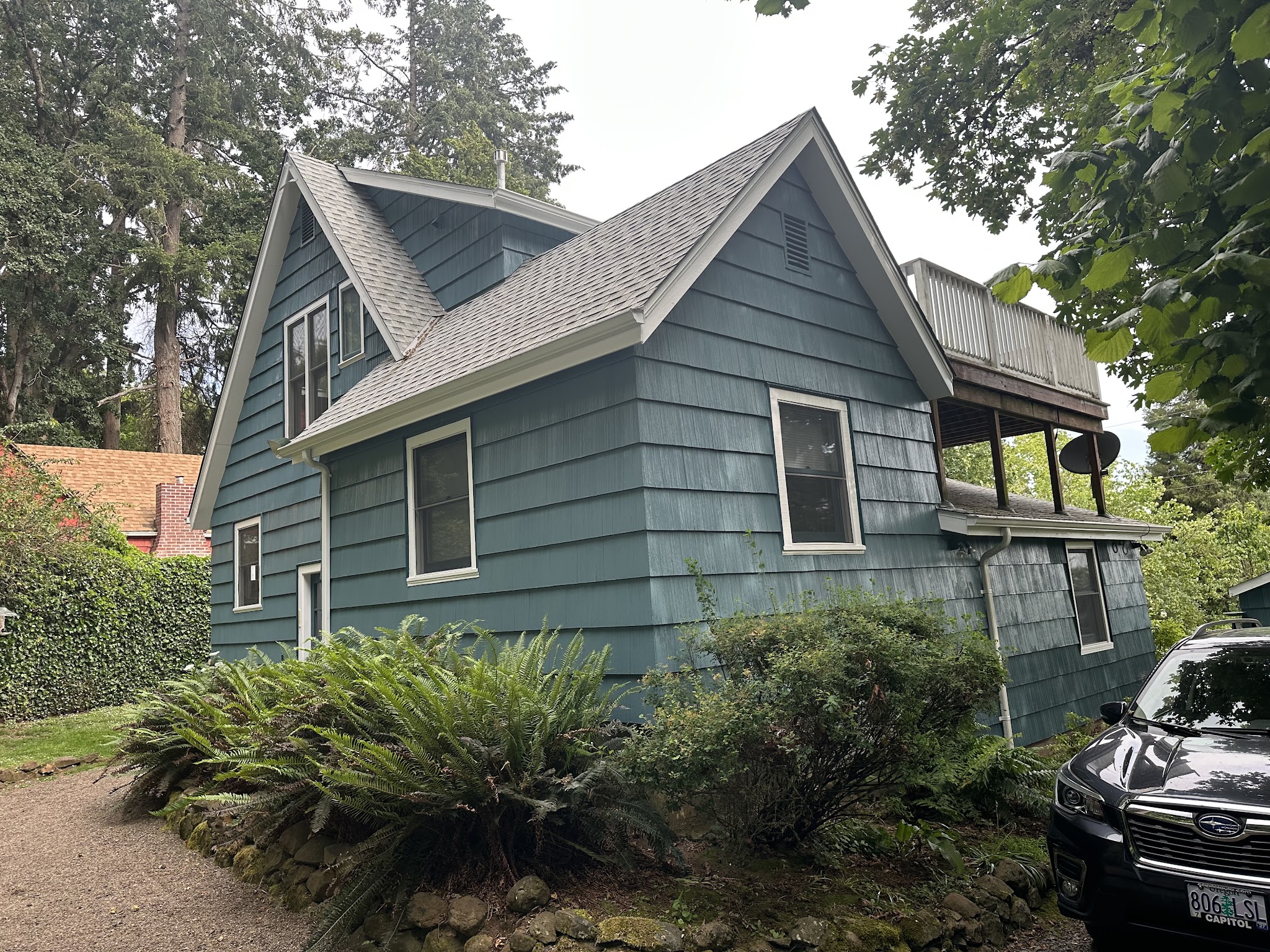 Cottage-style home in teal-blue shingles with white window trim among greenery
