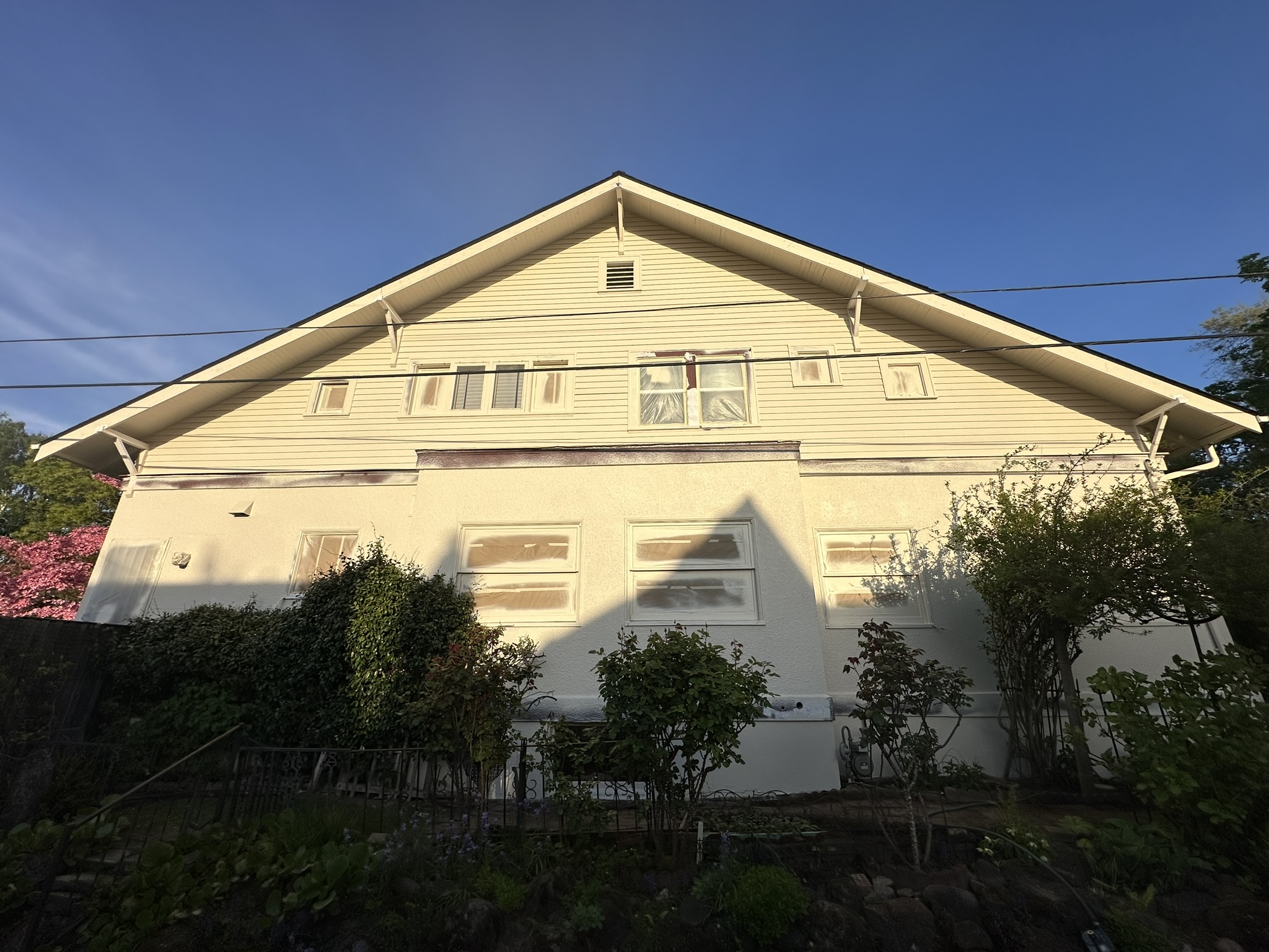 Cream craftsman-style house mid-job, windows papered and masked before painting